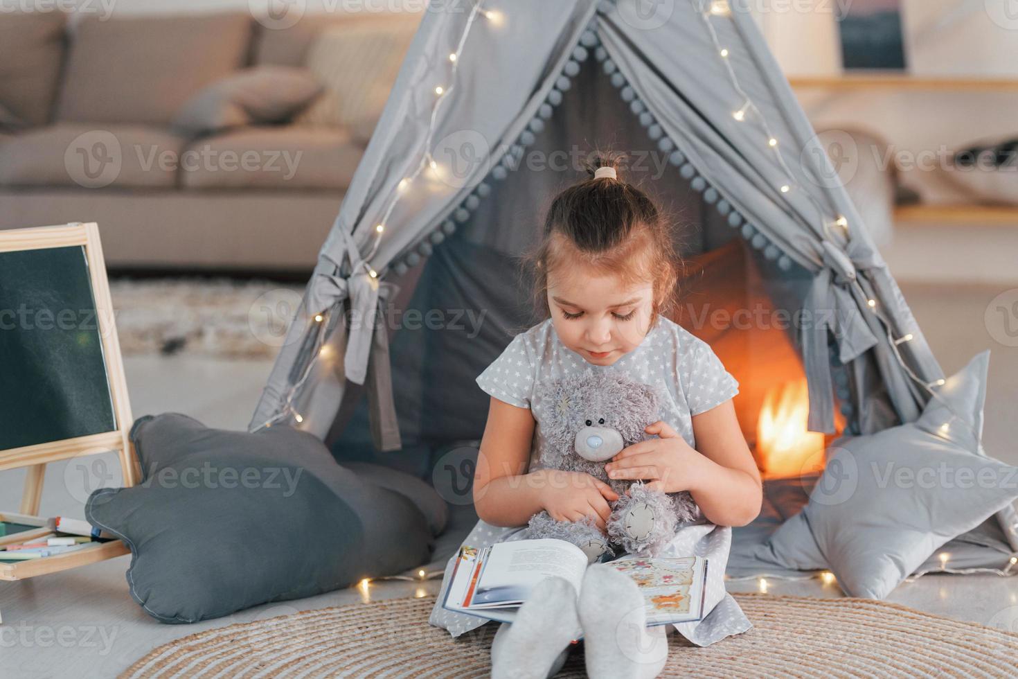 At daytime. Cute little girl playing in the tent that is in the domestic room photo