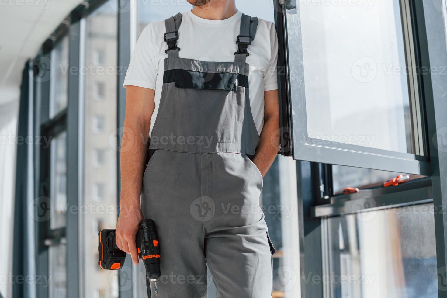 In grey uniform. Repairman is working indoors in the modern room photo