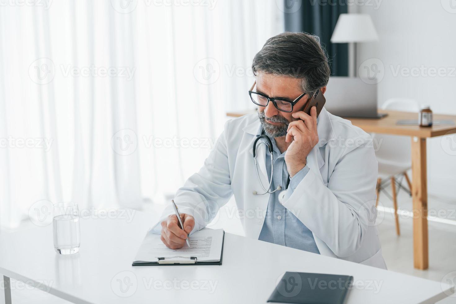 Man giving information by phone. Professional medical worker in white coat is in the office photo