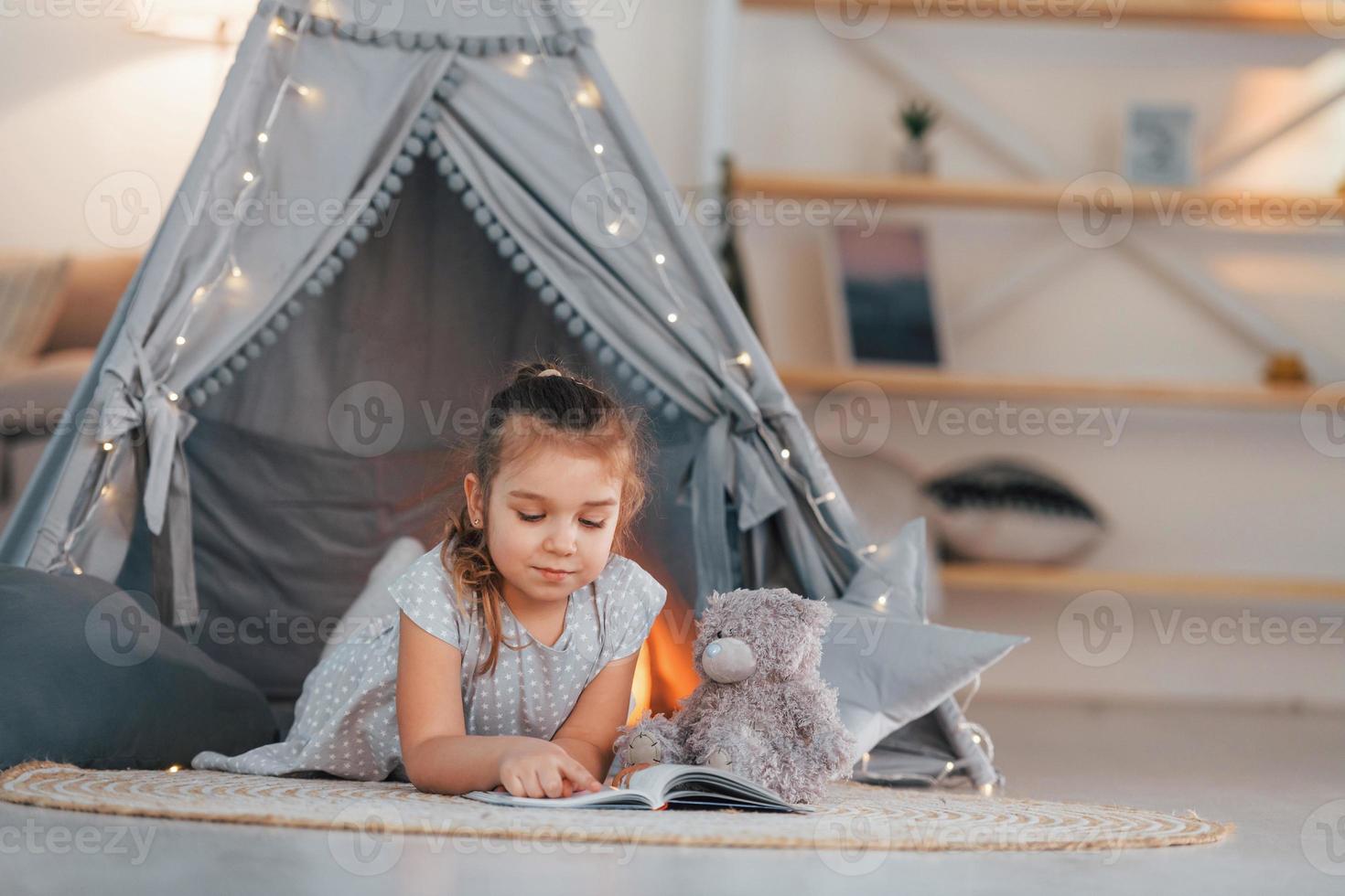Laying down on the ground. Cute little girl playing in the tent that is in the domestic room photo