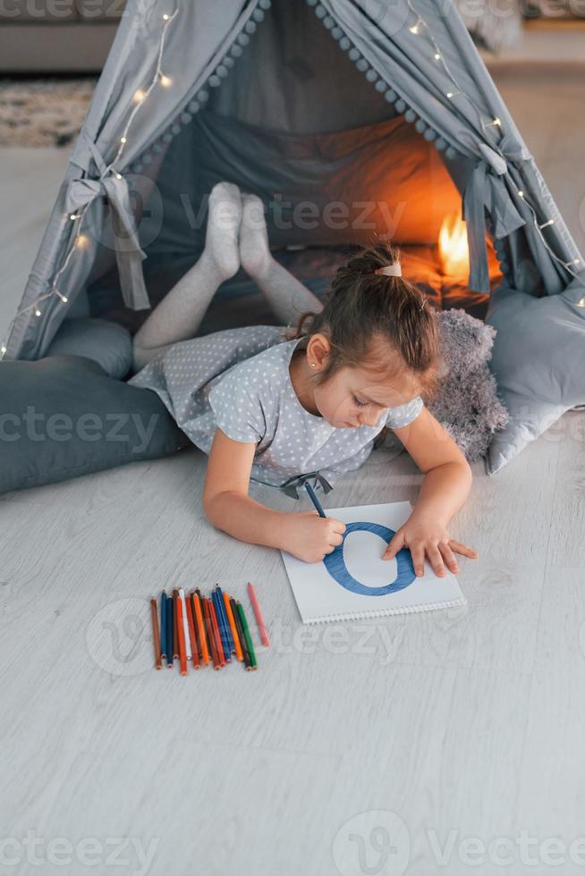 Writing letter. Cute little girl playing in the tent that is in the domestic room photo