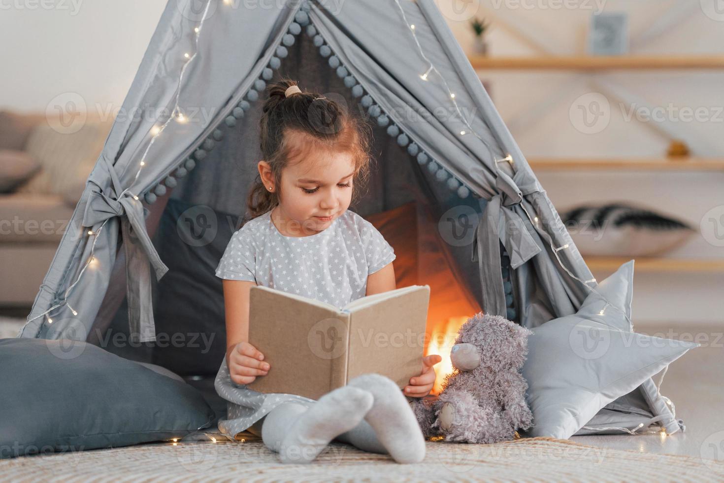 With book. Cute little girl playing in the tent that is in the domestic room photo