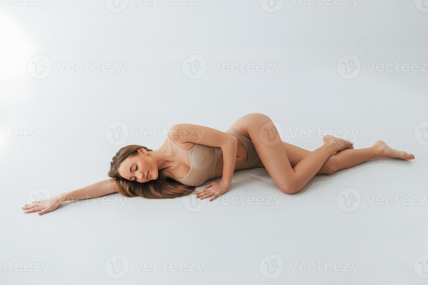 On the floor. Woman in underwear with slim body type is posing in the studio photo