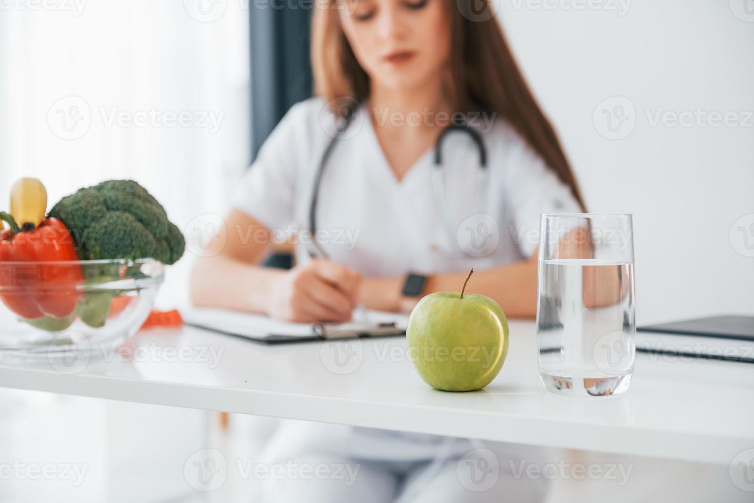 Woman writing information into the notepad. Professional medical worker in white coat is in the office photo
