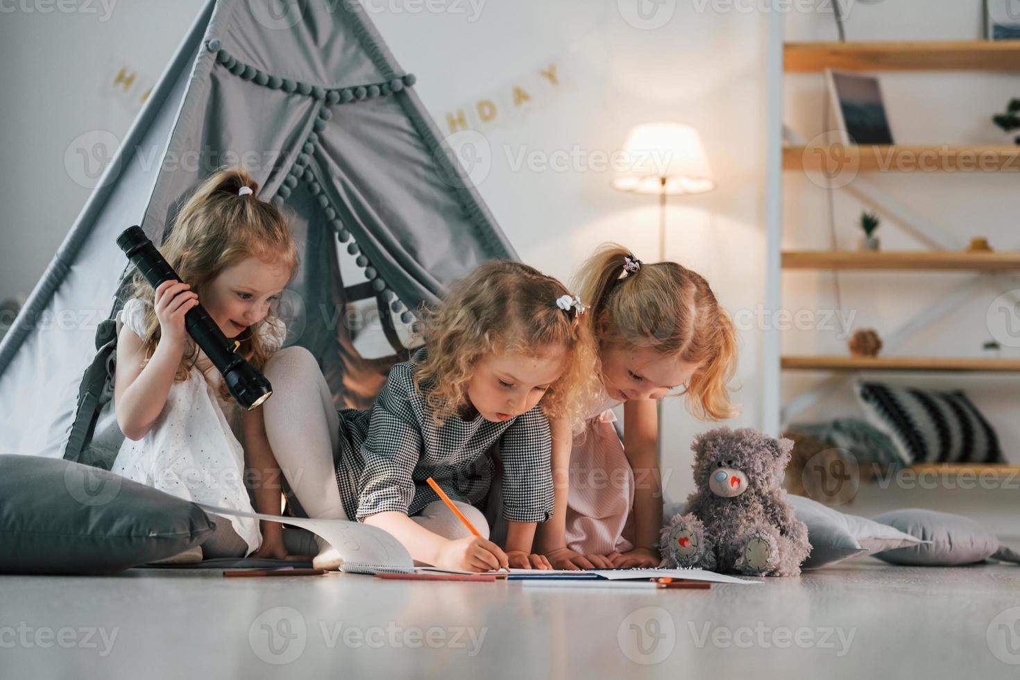 Girl holding flashlight. Other one draw on the ground with paper. Group of children is together at home at daytime photo