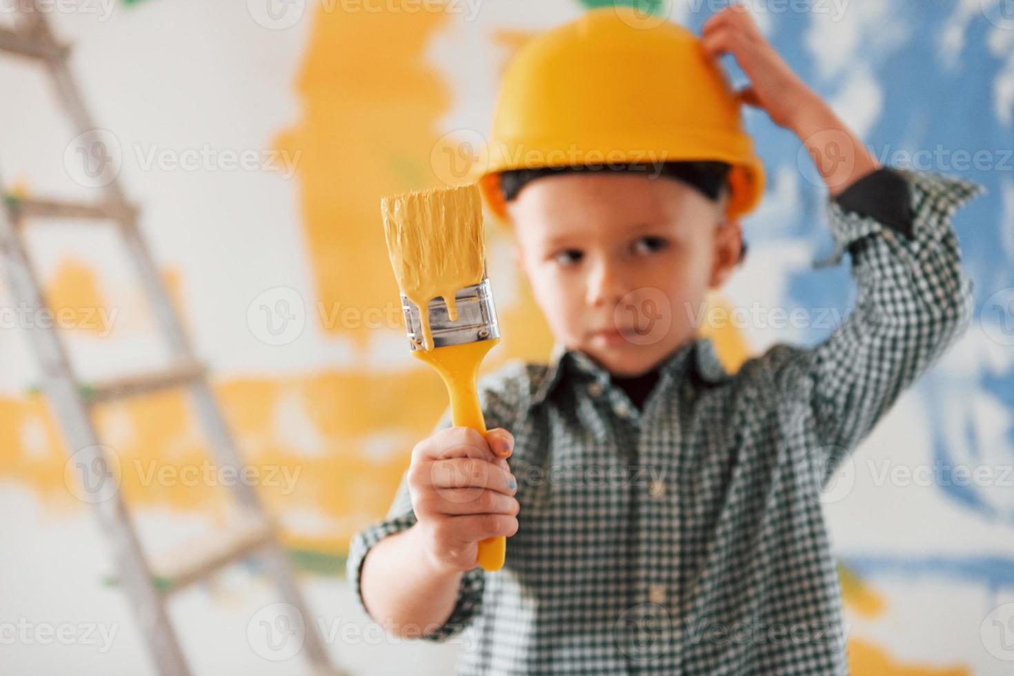 Blue and yellow colors behind. Conception of Ukraine and peace. Little boy painting walls in the domestic room photo