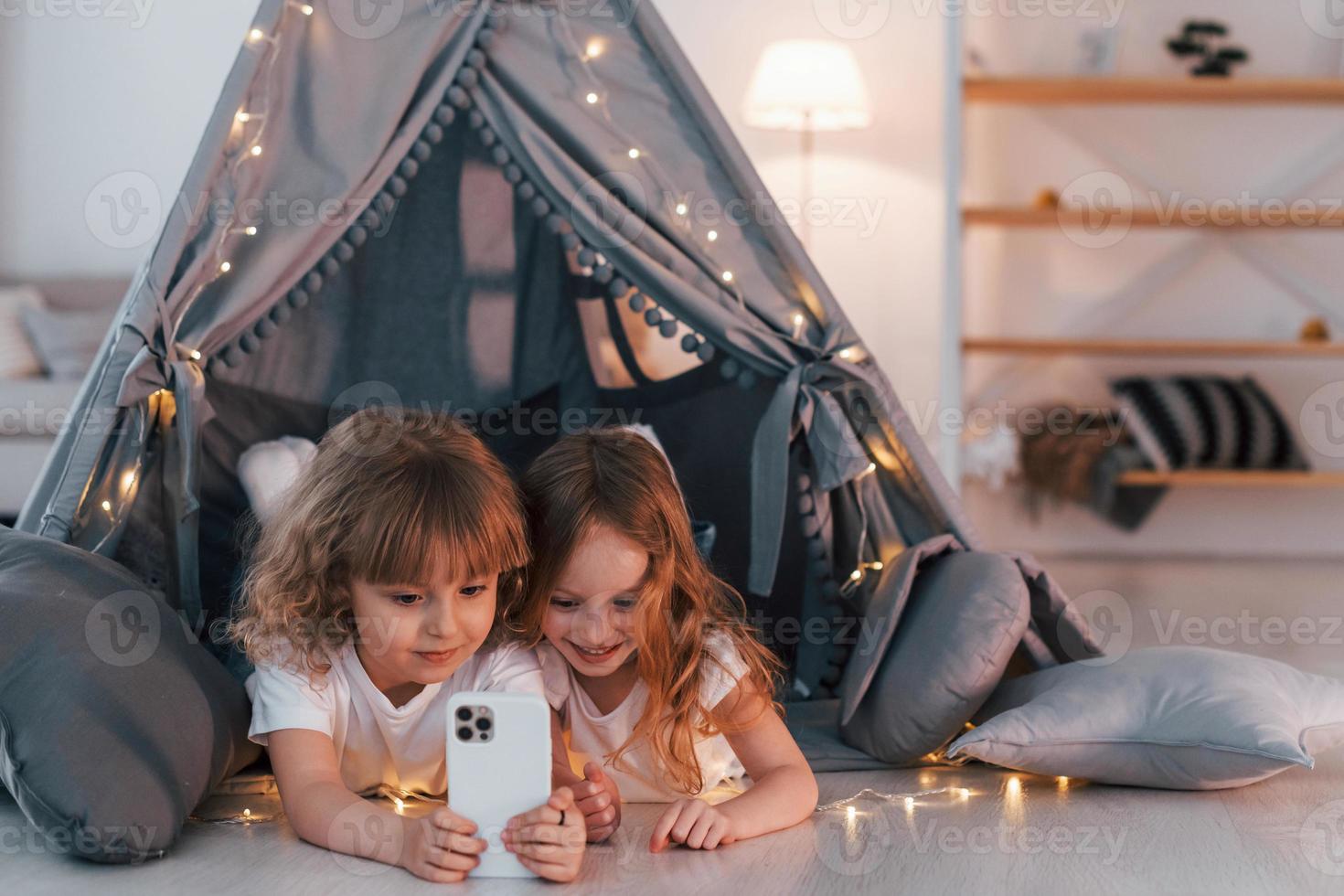 usando un teléfono inteligente. dos niñas pequeñas están juntas en la tienda en la habitación doméstica foto