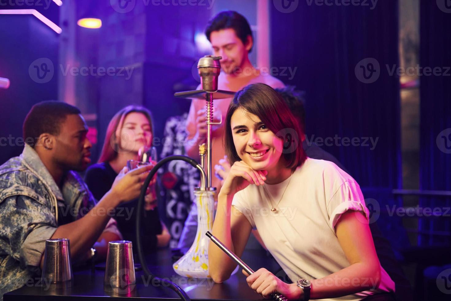 mujer fumando narguile. grupo de amigos divirtiéndose juntos en la discoteca foto