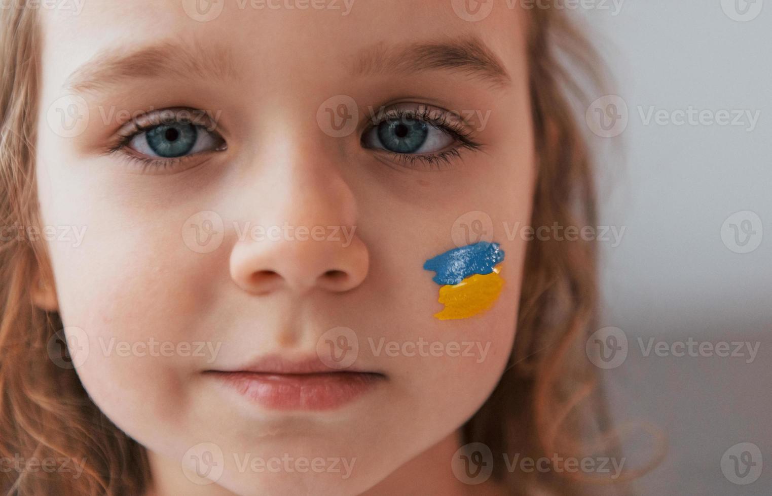 Close up view. Portrait of little girl with Ukrainian flag make up on the face photo