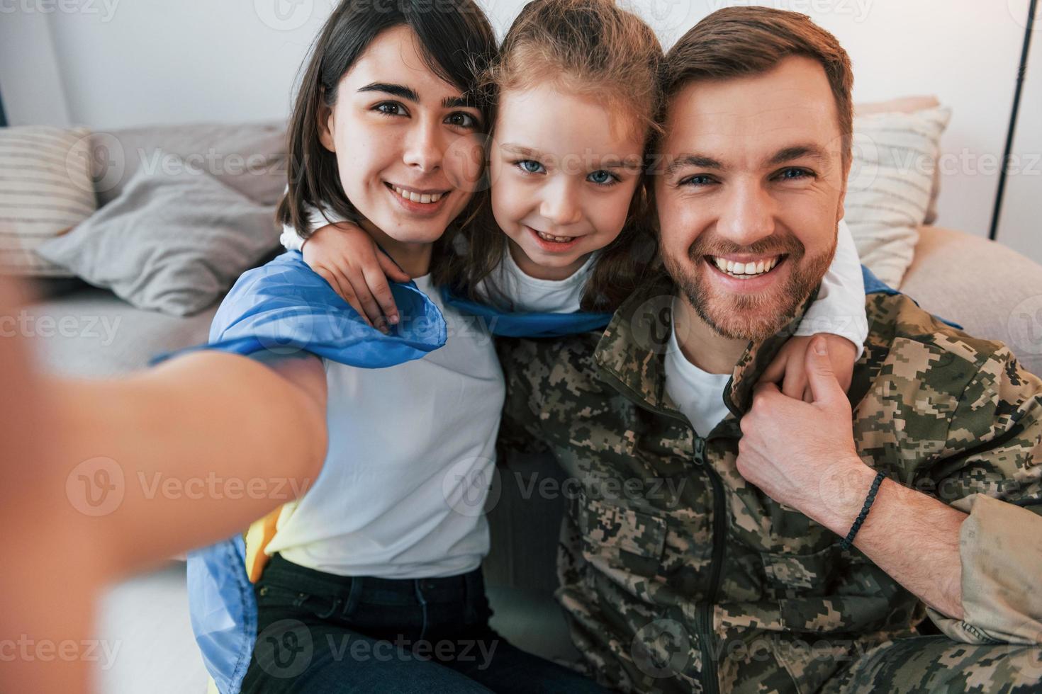 Making selfie. Soldier in uniform is at home with his wife and daughter photo