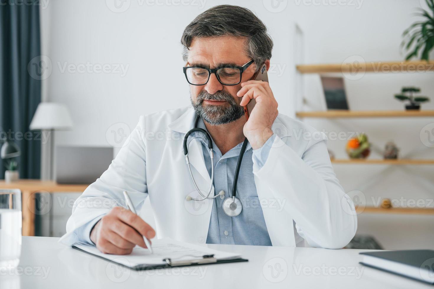 Man giving information by phone. Professional medical worker in white coat is in the office photo