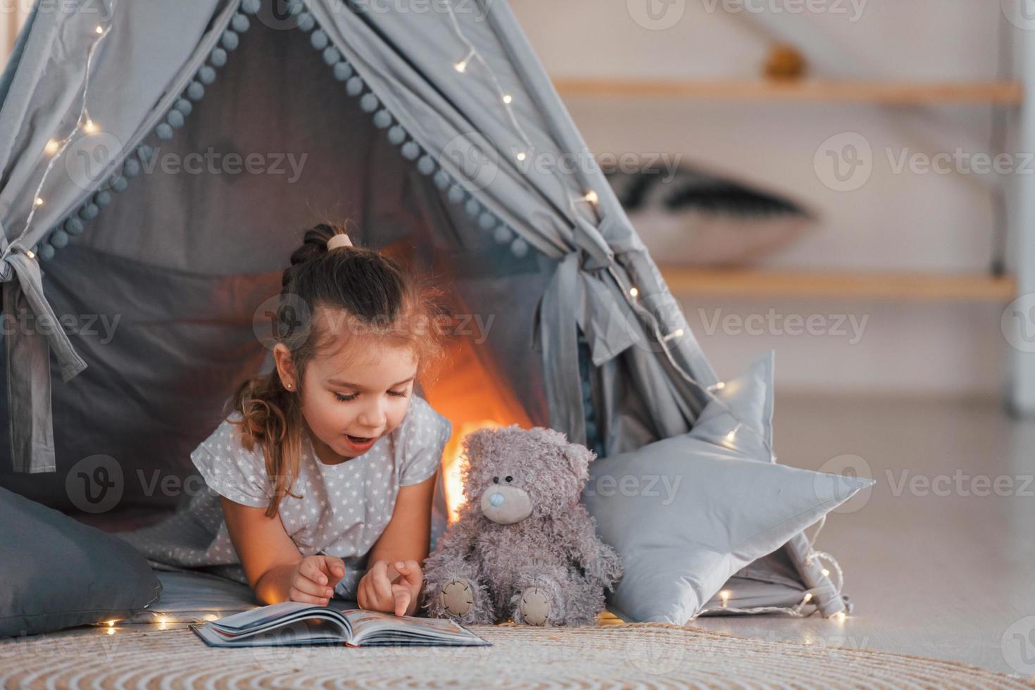 Lamp is behind. Cute little girl playing in the tent that is in the domestic room photo