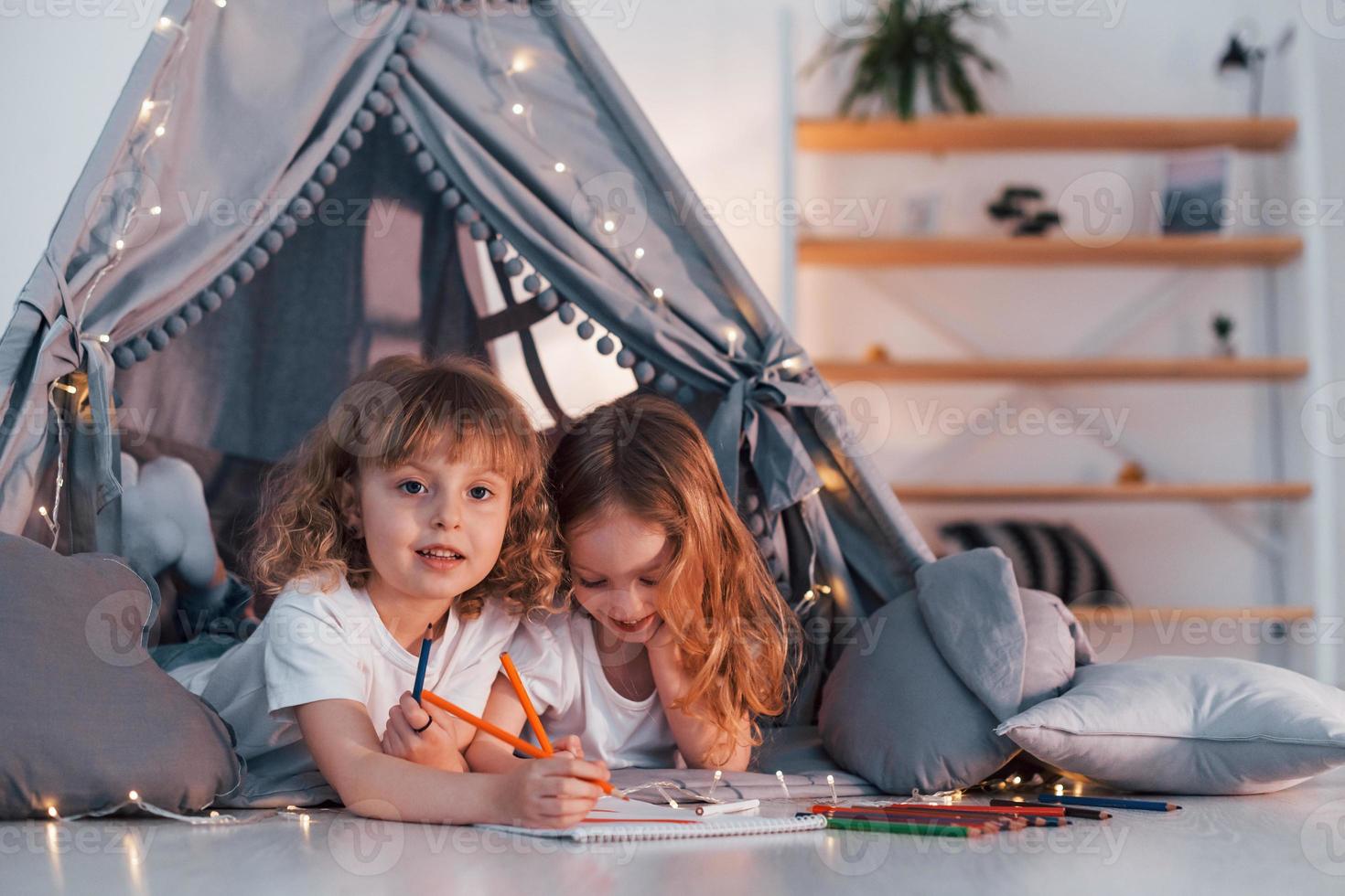 Learning to write and draw. With paper and pencils. Two little girls is in the tent in domestic room together photo
