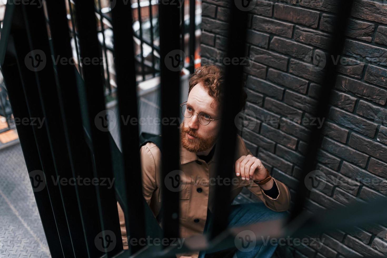 View through steel railings. Man in khaki colored jacket and in jeans is on the stairs on the building outdoors photo