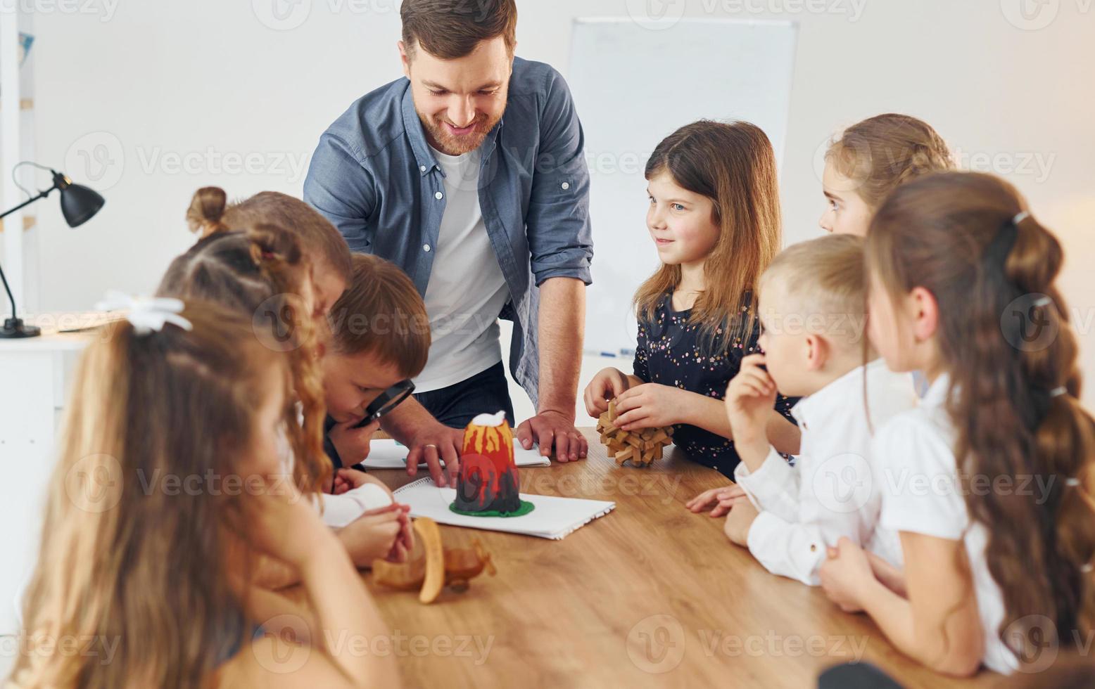 Looking at the little volcano model. Group of children students in class at school with teacher photo