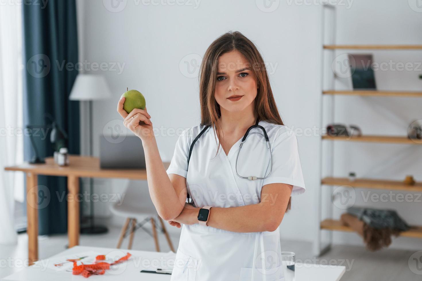 Woman holding an apple. Professional medical worker in white coat is in the office photo
