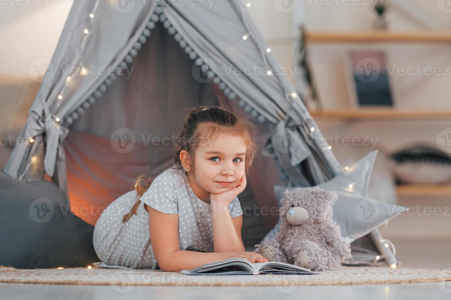 Laying down on the ground. Cute little girl playing in the tent that is in the domestic room photo