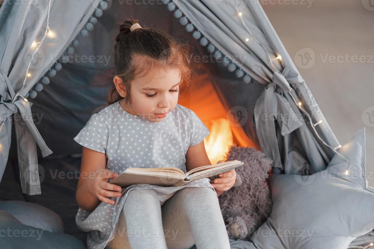 With book. Cute little girl playing in the tent that is in the domestic room photo