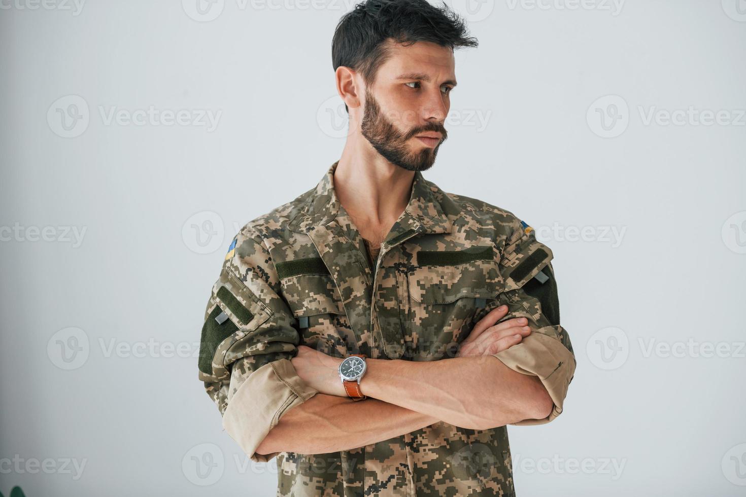 brazos cruzados. soldado en uniforme está de pie en el interior contra la pared blanca foto