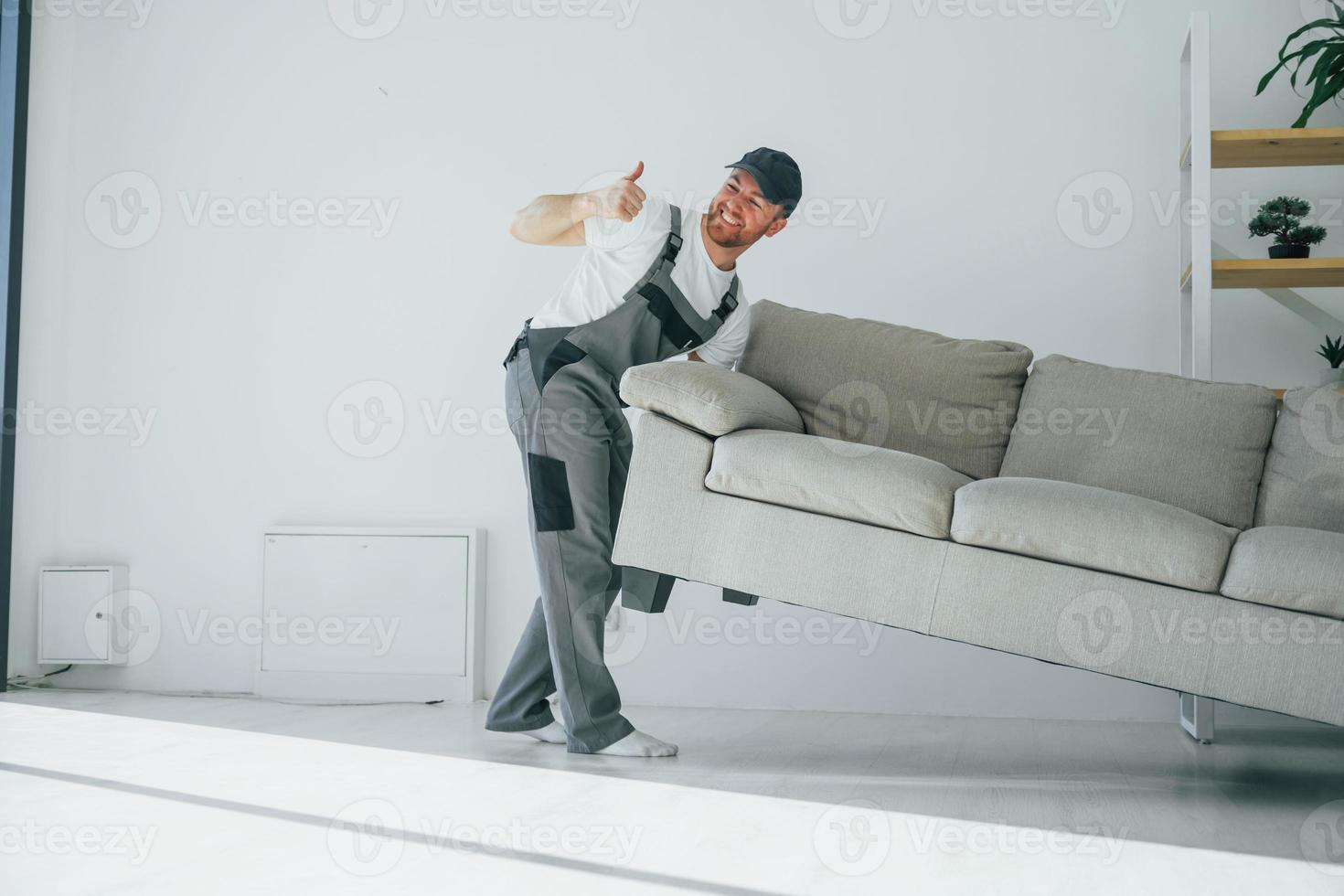 Lifting the sofa. Repairman is working indoors in the modern room photo