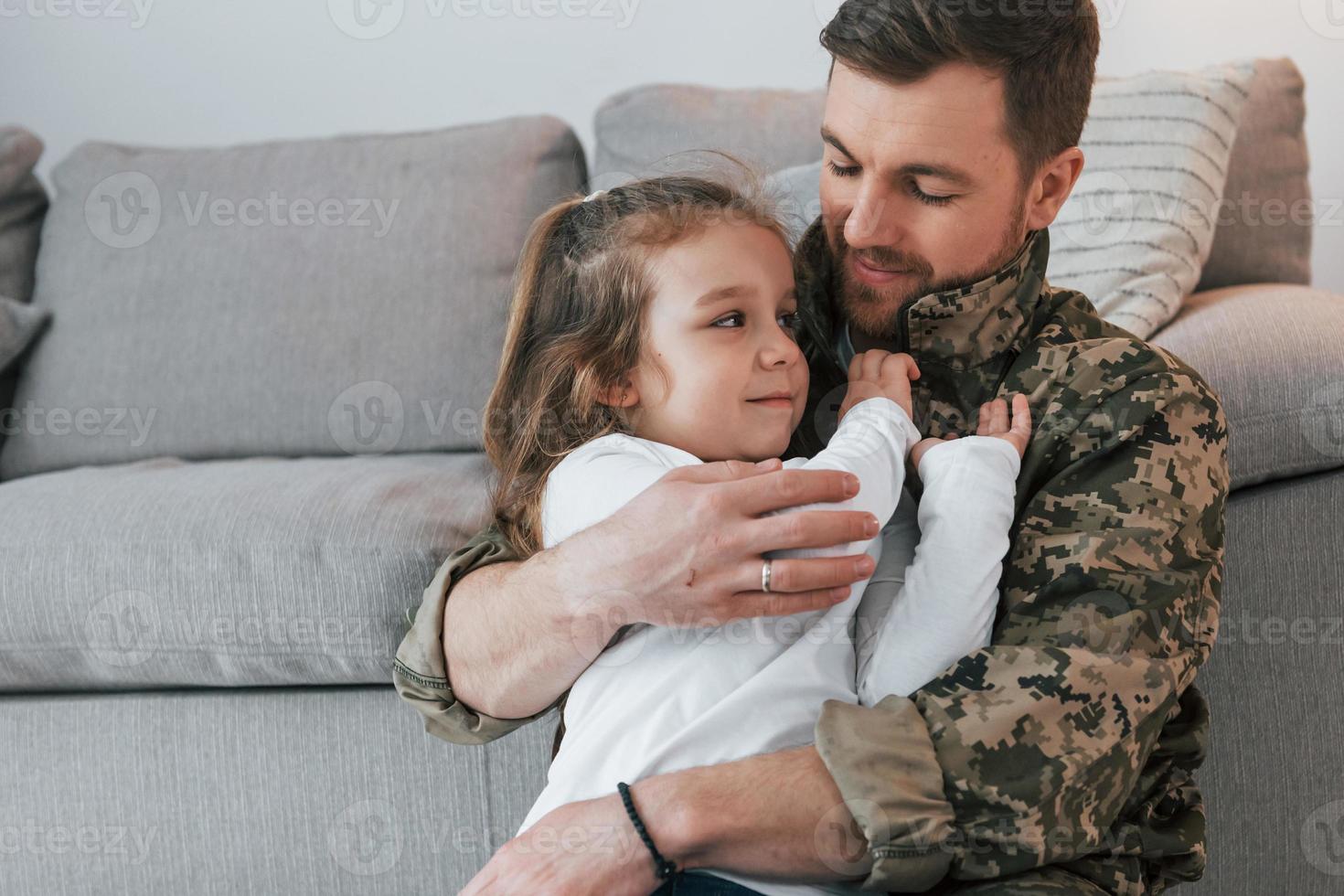 Conception of defending and safety. Soldier in uniform is at home with his little daughter photo