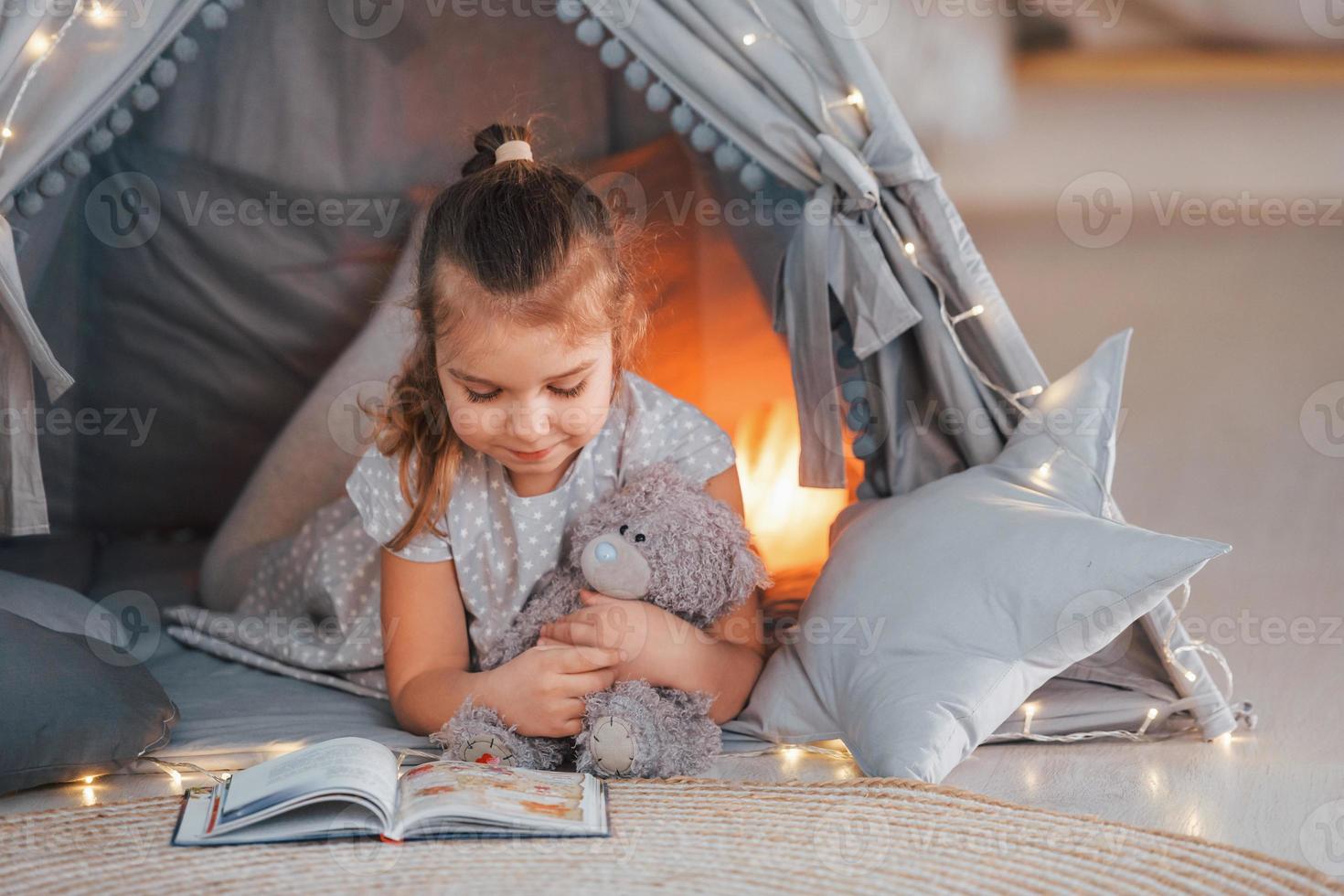 Lamp is behind. Cute little girl playing in the tent that is in the domestic room photo