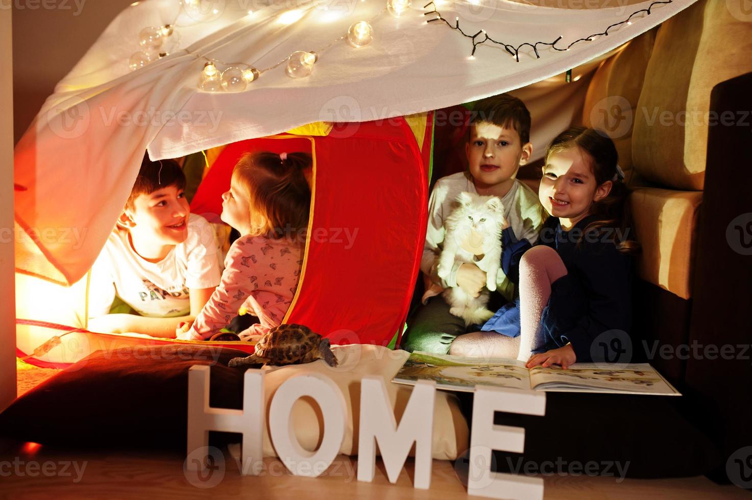 Playing kids with kitty in tent at night home. Hygge mood. photo