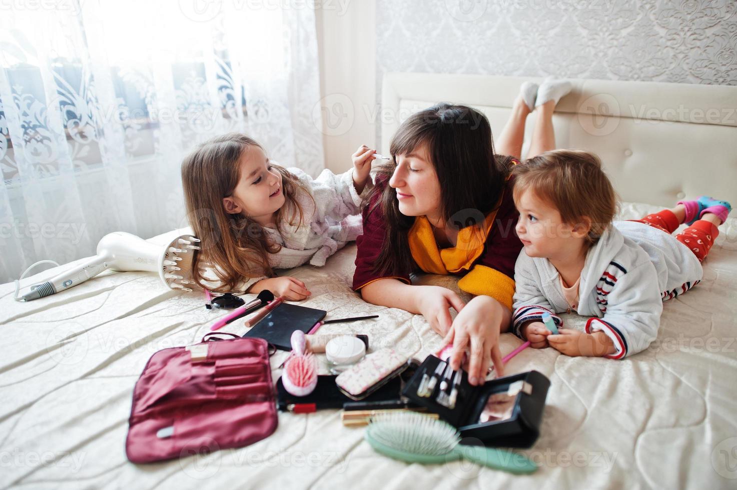 Mother and daughters doing makeup on the bed in the bedroom. photo