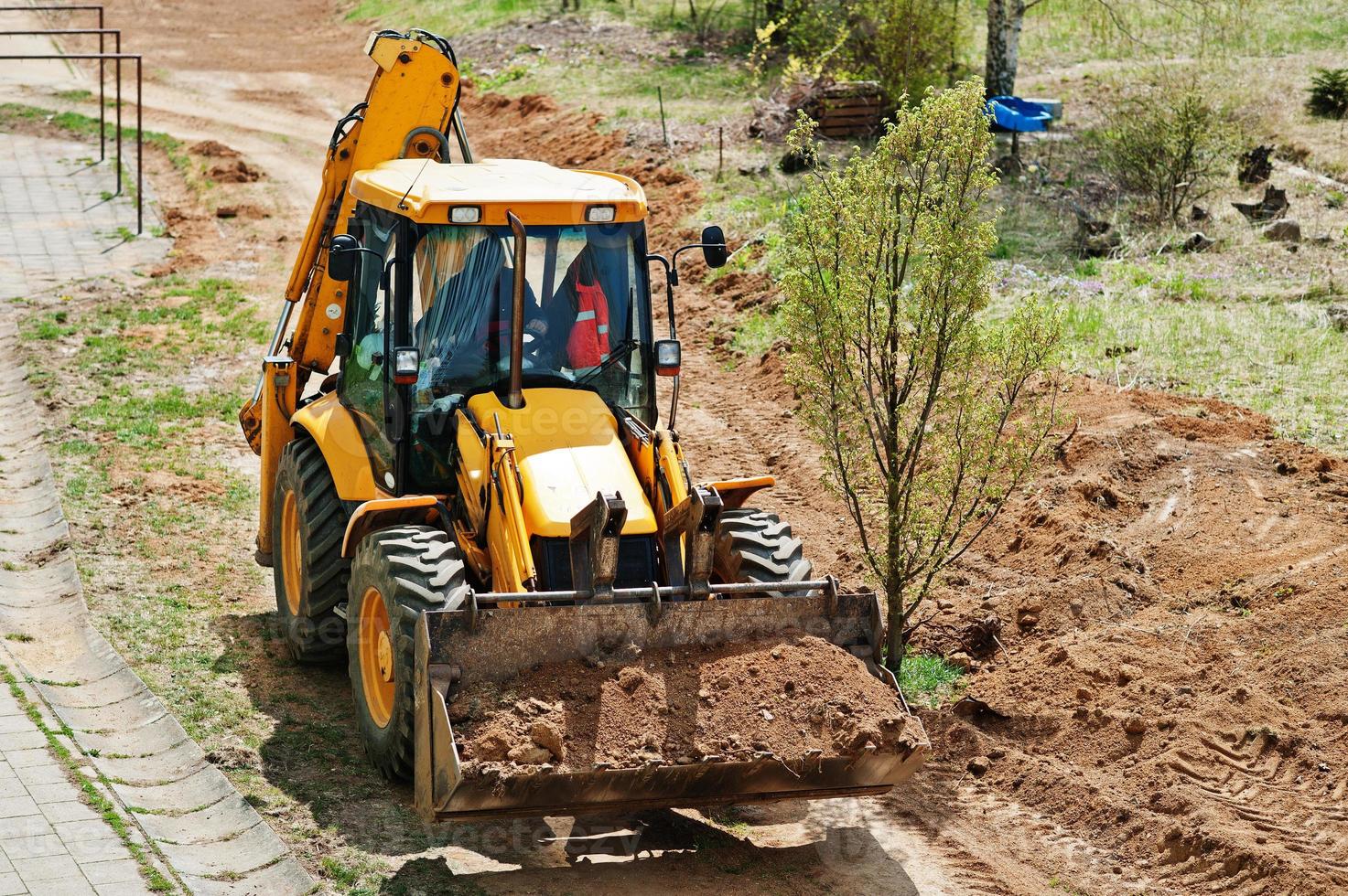 Tractor bucket levels a trench near the house photo