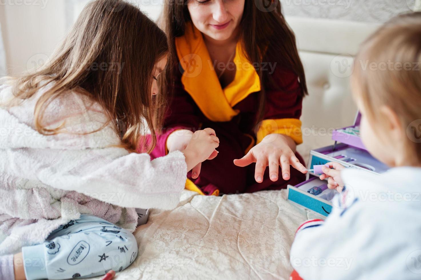 Mother and daughters doing manicures on the bed in the bedroom. photo