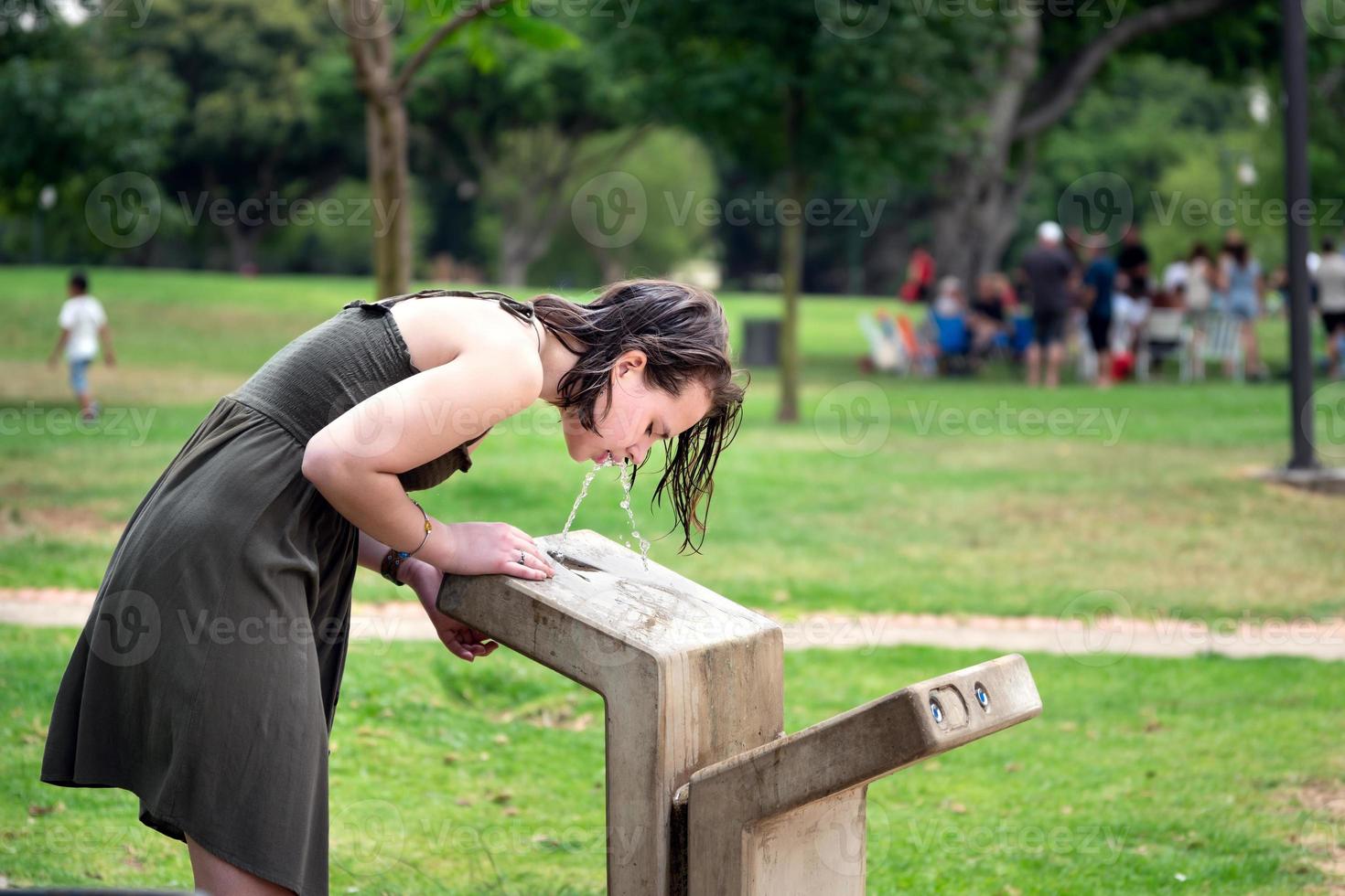 Teenage girl drinking water from an outdoor water fountain photo