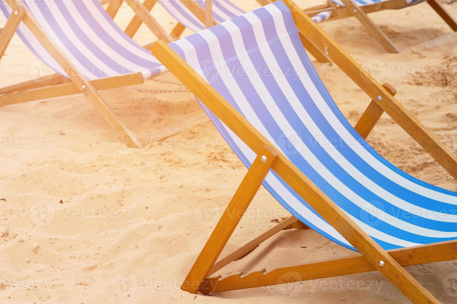 Blue and white striped deckchairs standing on sand on a beach photo