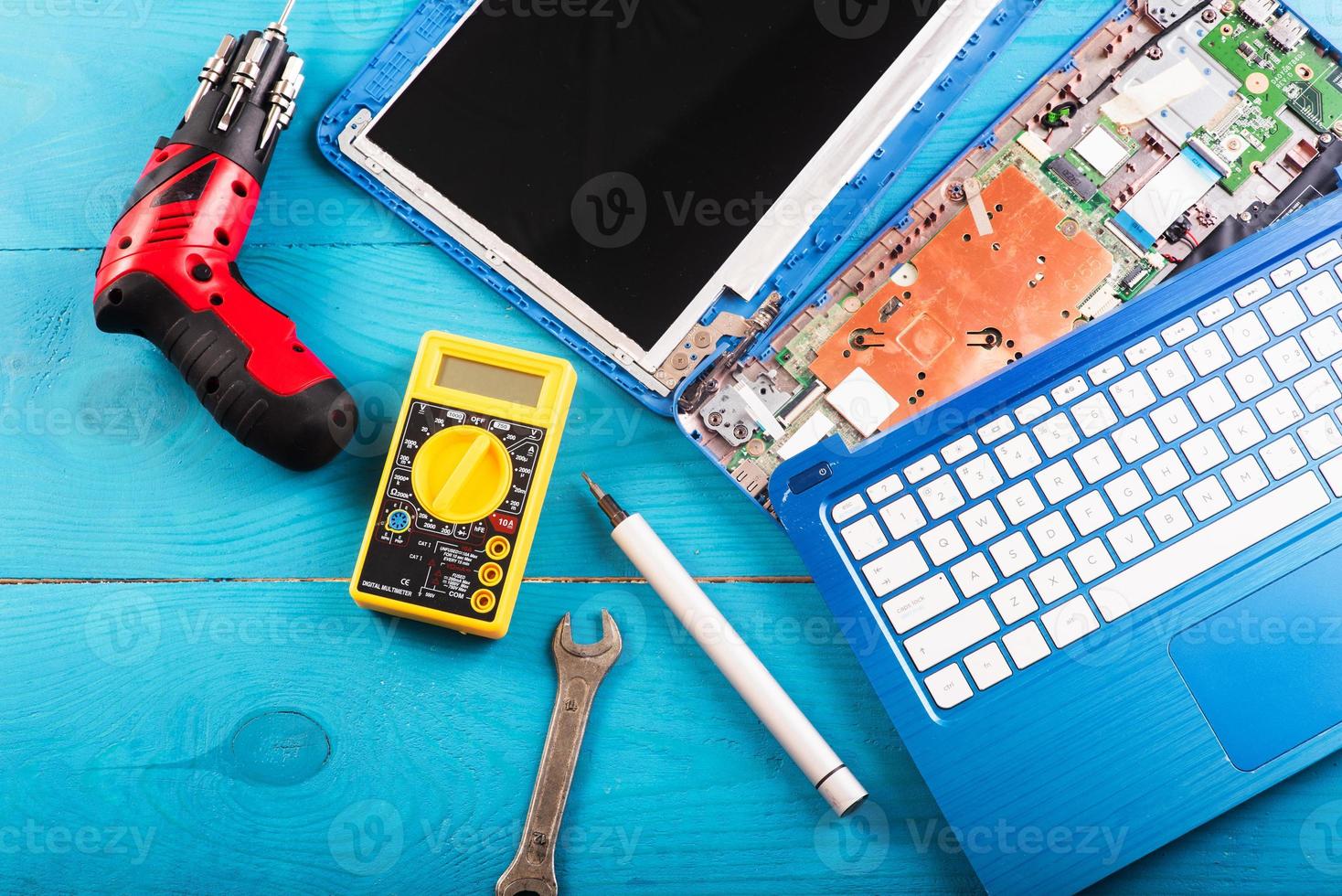 el asistente repara la computadora portátil con herramientas y manos en la mesa de madera azul. vista superior foto