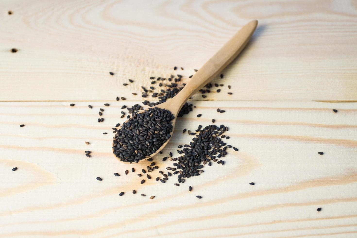 Black sesame seeds in wooden spoon pile on wood table photo