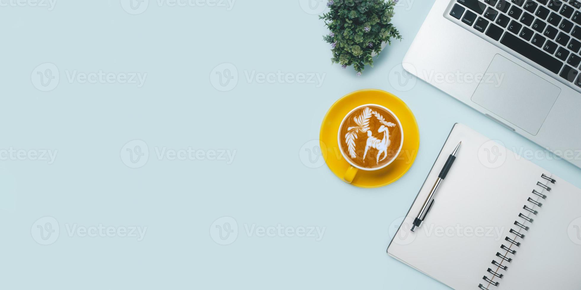 Office desk with computer, Pen, Notebook, Cup of coffee on blue background, Top view with copy space, Mock up. photo