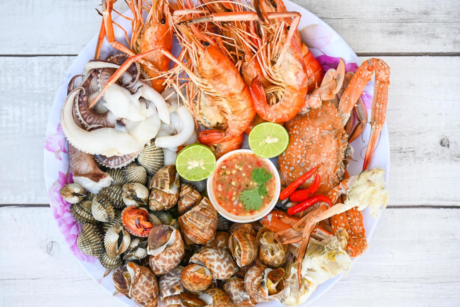 plato de mariscos con camarones mariscos cangrejo calamar berberecho manchado de babilonia con salsa de mariscos chile lima limón servir en la mesa de comedor, camarones langostinos menú buffet de mariscos comida cocinada foto