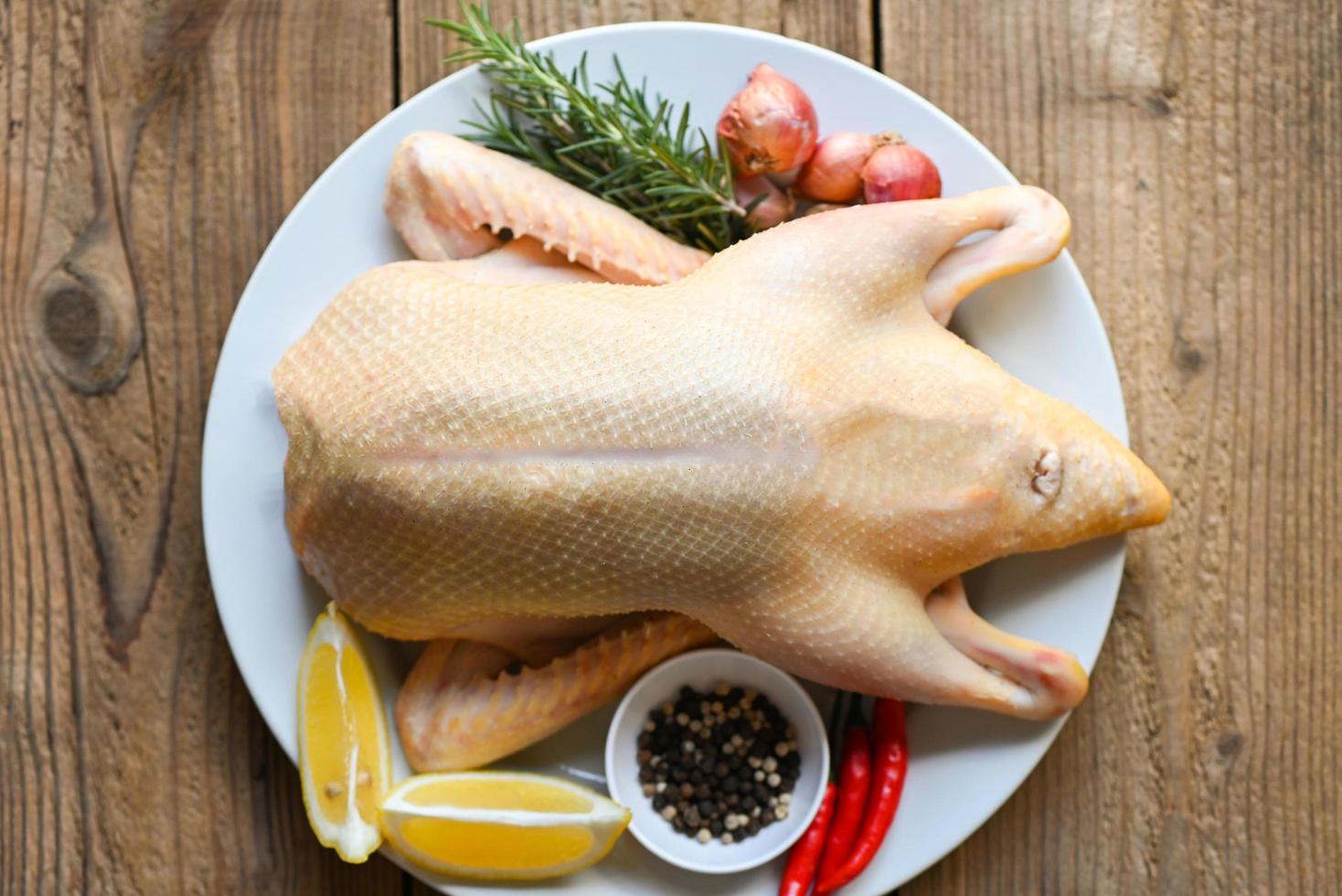 raw duck with spices ready to cook on wooden background , fresh duck meat on plate for food , whole duck and lemon rosemary chili garlic - top view photo