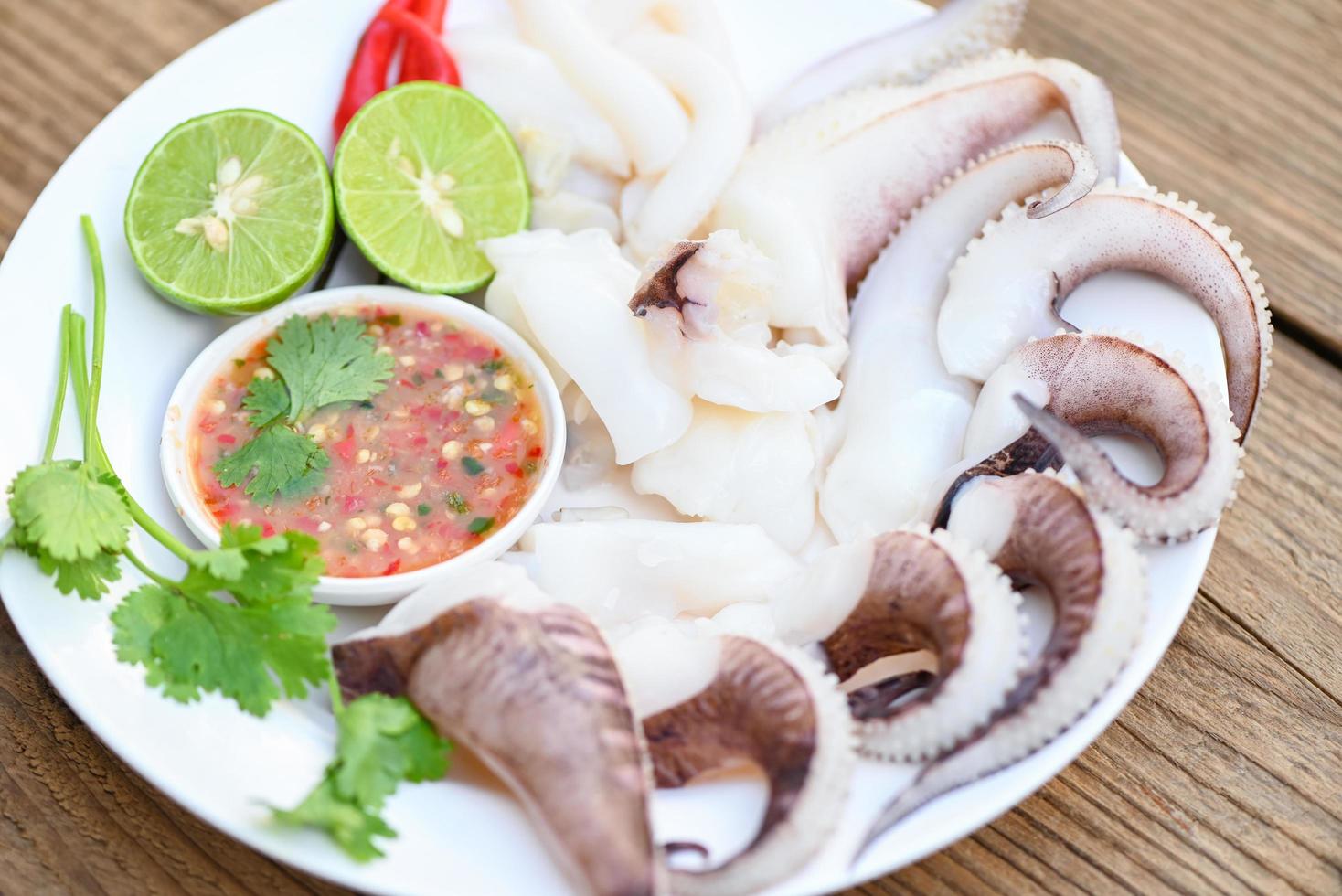 seafood plate squid food on white plate, Fresh squid cooked boiled steam with vegetable salad lemon lime and seafood sauce chili sauce serve on table, octopus tentacles cuttlefish ocean gourmet photo