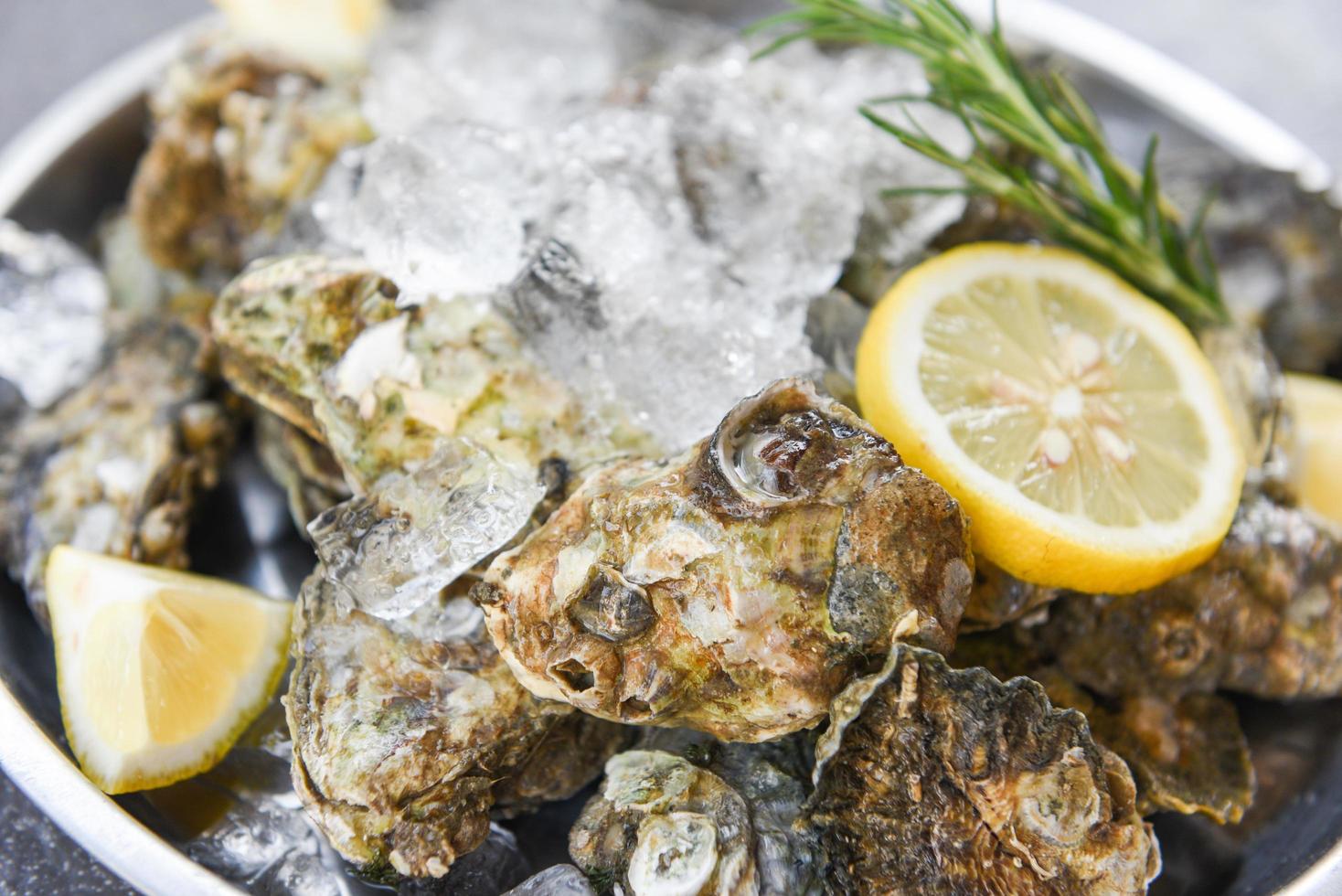 concha de ostra con hierbas, especias, limón, romero, mesa servida y hielo, marisco saludable, cena de ostras crudas en el restaurante, comida gourmet, ostras frescas, mariscos en un plato de fondo negro foto