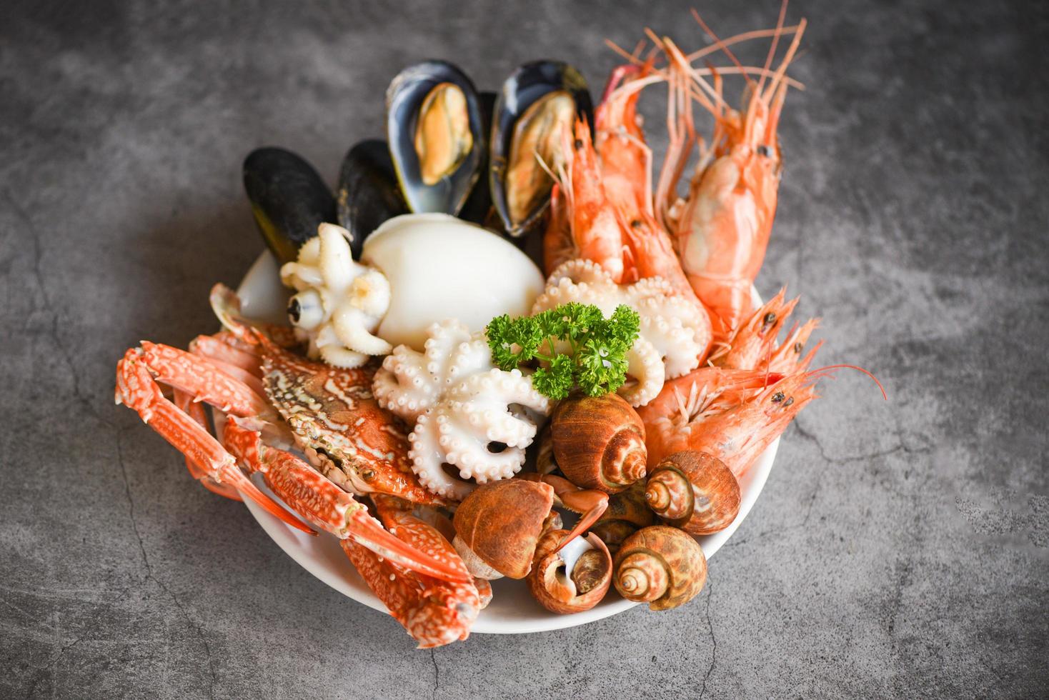Seafood shrimps prawns squid mussels spotted babylon shellfish crab  on plate and dark background - Cooked food served seafood buffet concept photo