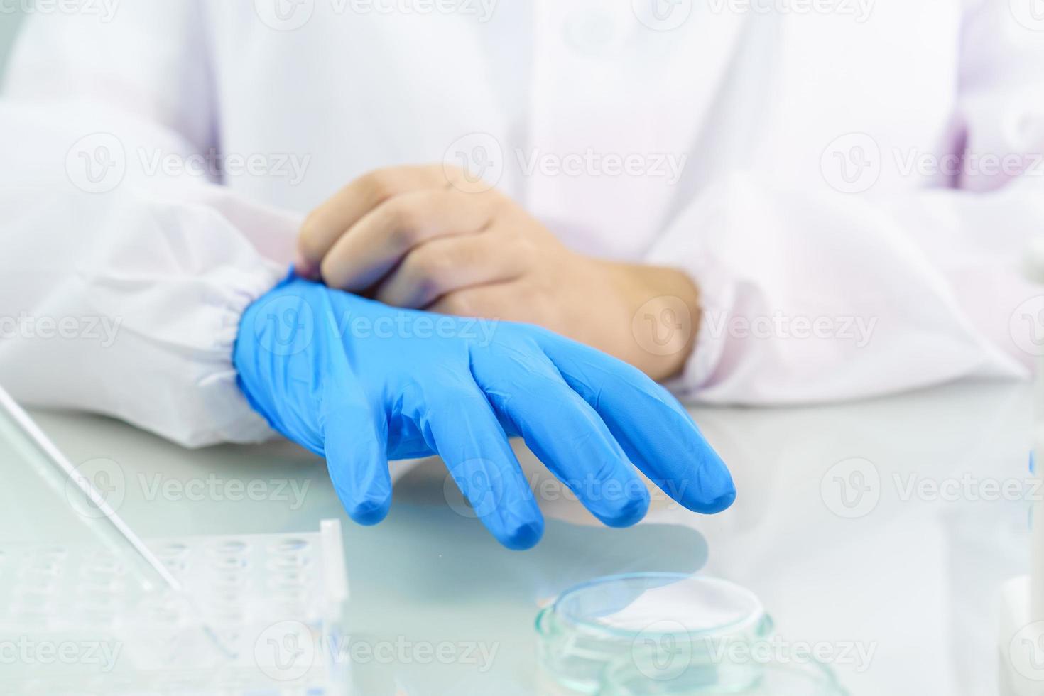 Manos científicas poniéndose guantes de látex azul de nitrilo en una bata de laboratorio usando guantes de nitrilo foto