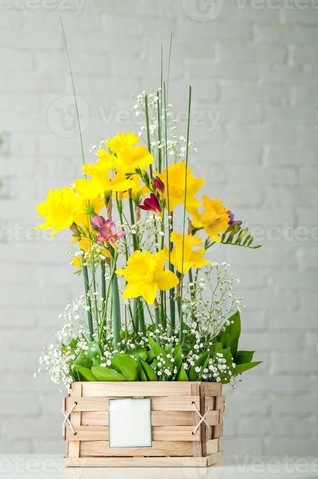 A vertical shot of a beautiful composition with daffodils and pink freesia in a wooden box photo