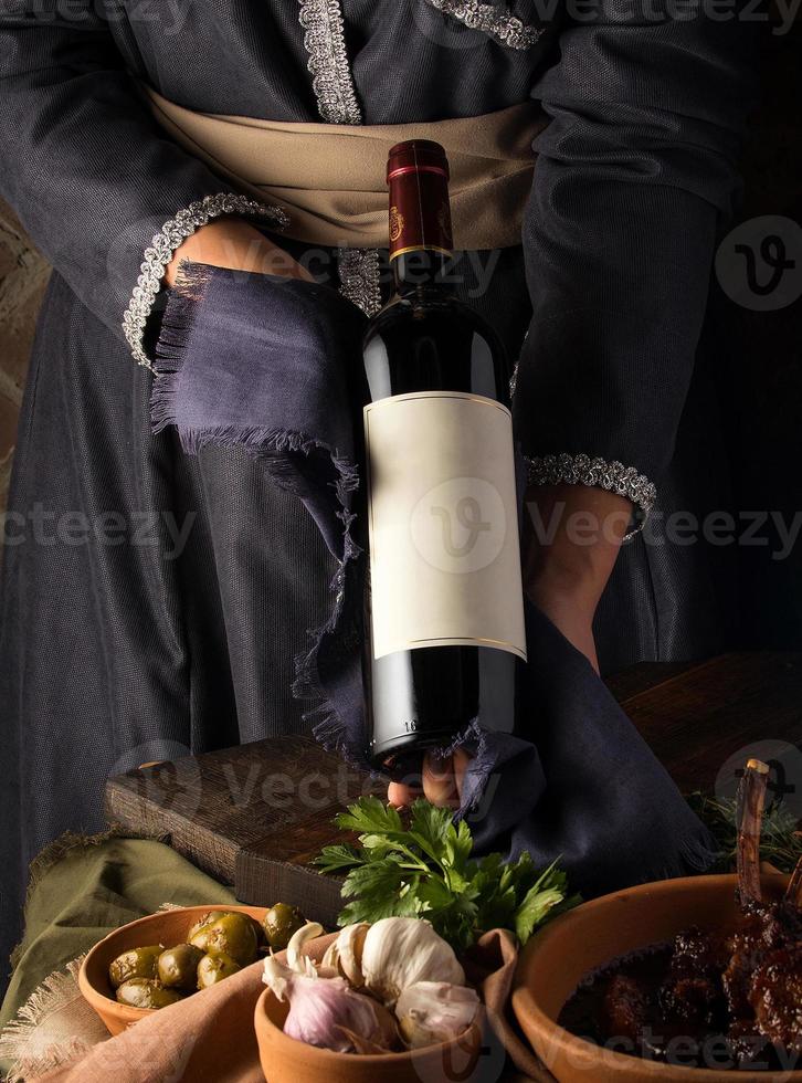 A vertical shot of a person in a traditional costume showing a wine bottle photo