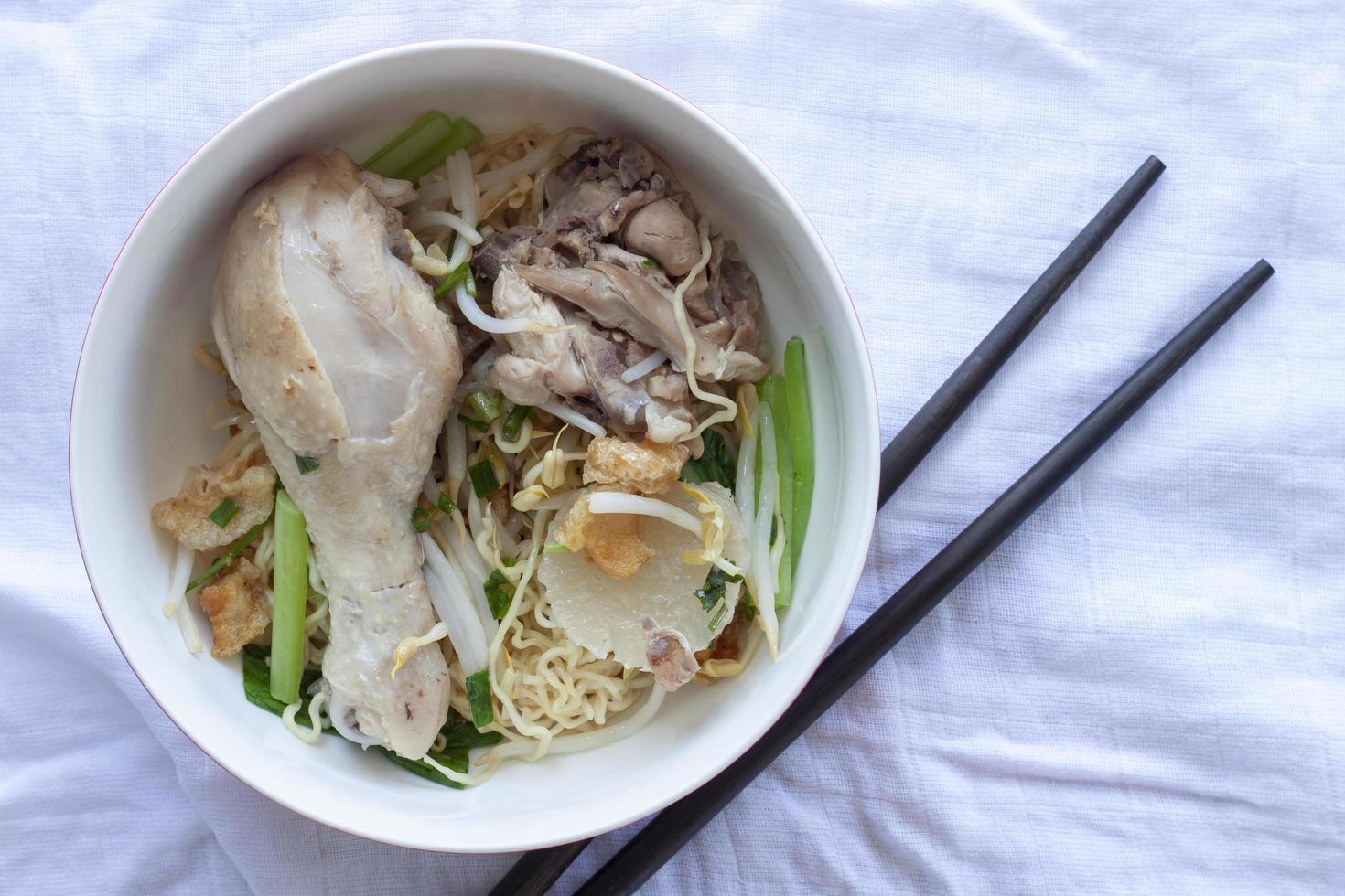 Egg Noodle with Chicken Drum Stick in a bowl and chopsticks placed on a white tablecloth. photo