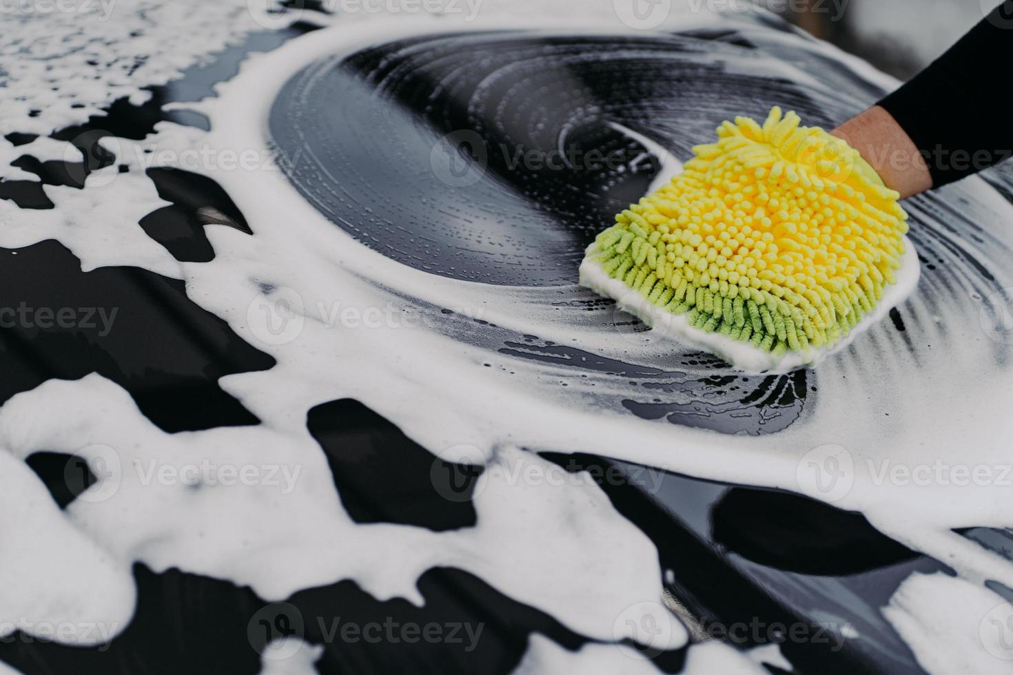 Mans hand washing black car with cloth and soap bubbles. Cleaning automobile. Selective focus. Carwsh concept. photo