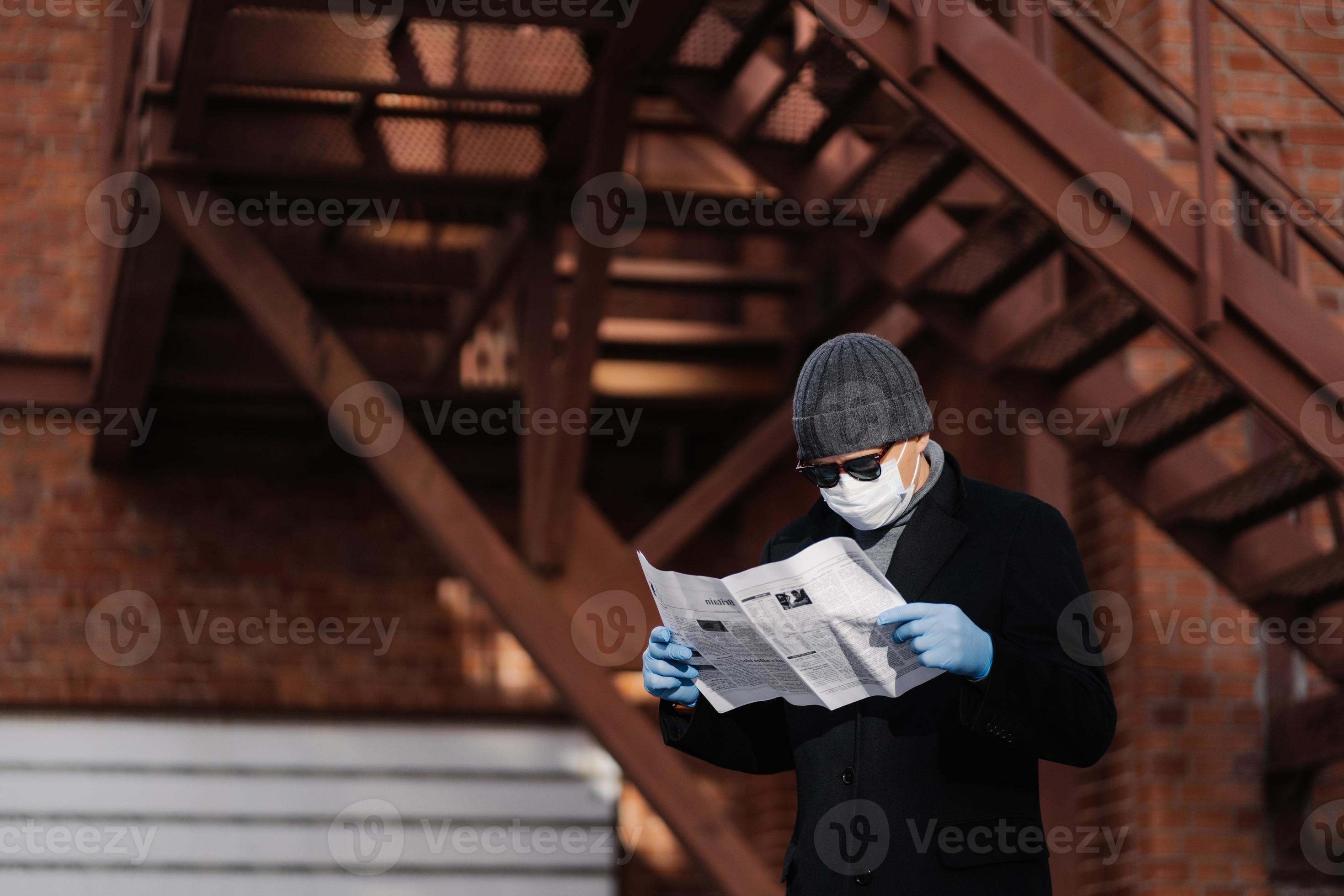 Concentrated Man Wears Sunglasses And Coat Medical Mask Protective Rubber Gloves Reads Fresh News About Coronavirus Spreading From Newspaper Poses Against Blurred Background With Stairs Stock Photo At Vecteezy