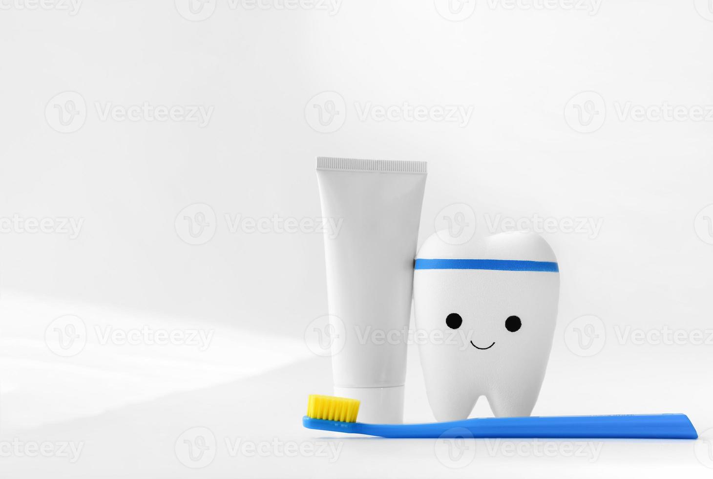diente de juguete, cepillo de dientes azul y pasta de dientes sobre fondo blanco foto