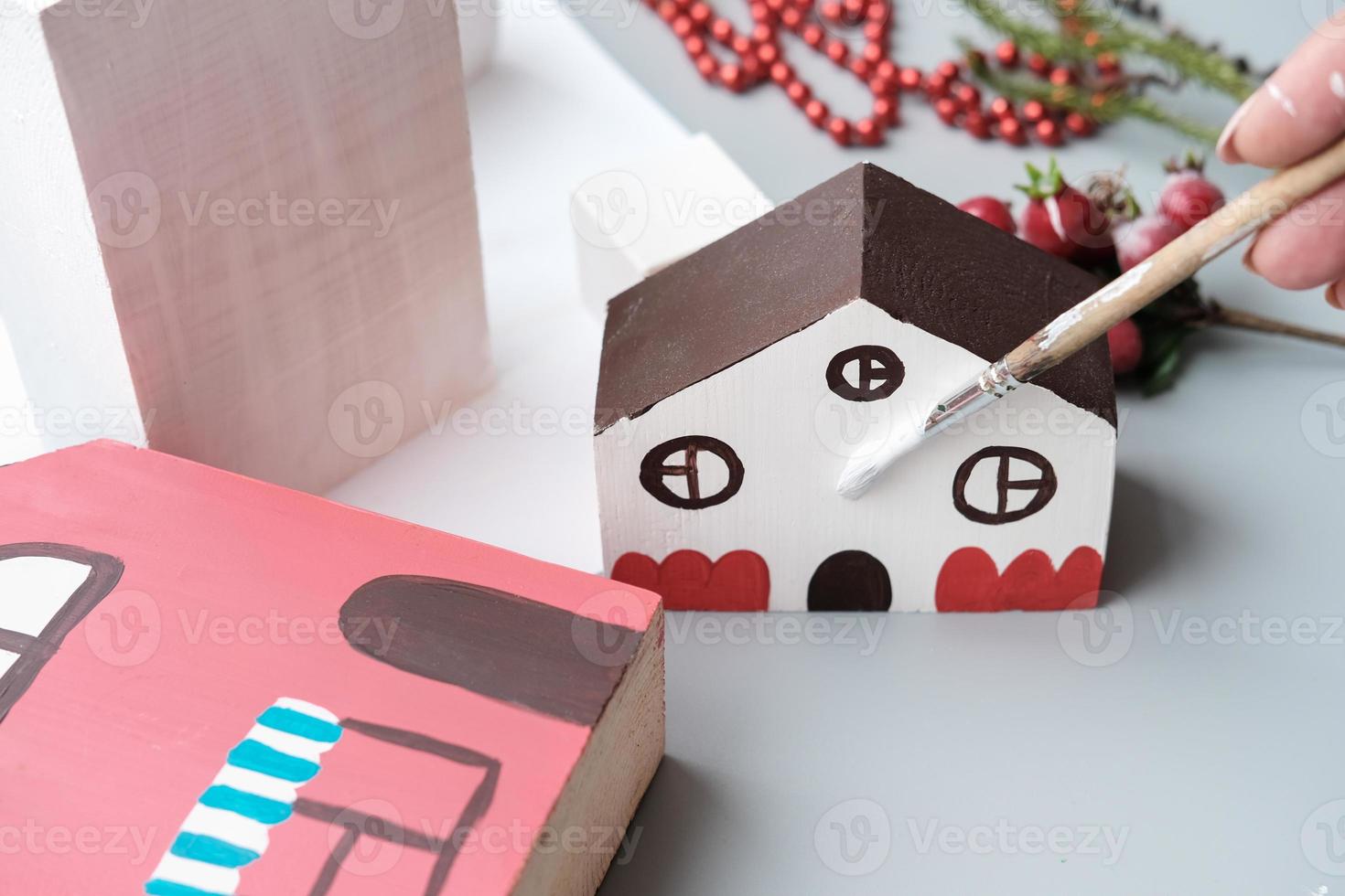 female hand holding paint brush and painting toy wooden house photo
