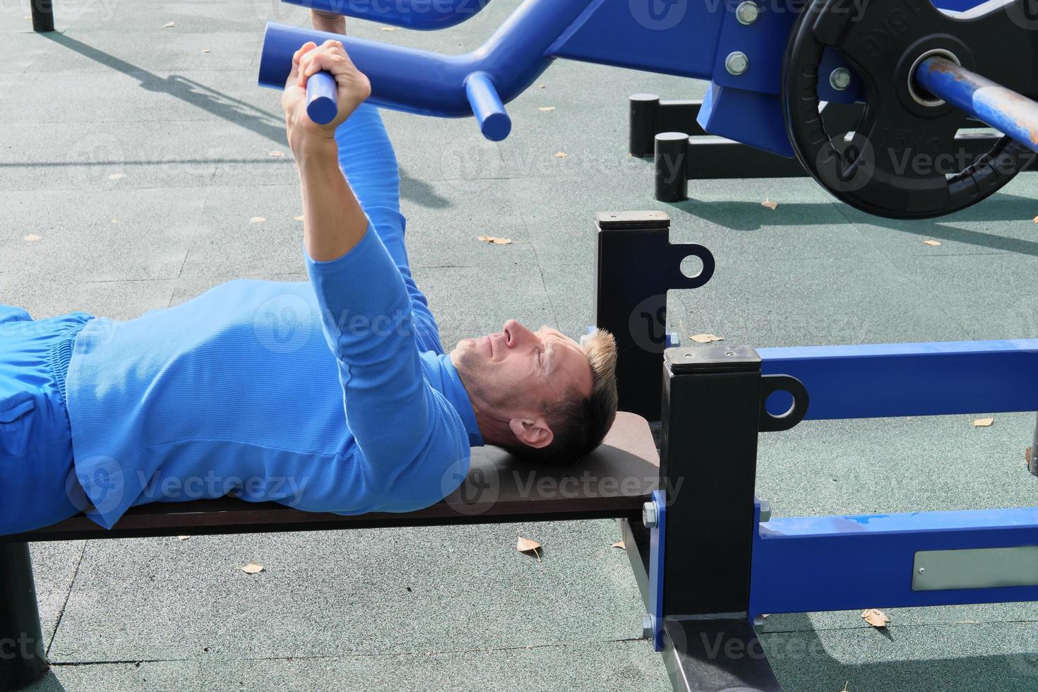 sporty slim man doing bench press using outdoors gym equipment. photo