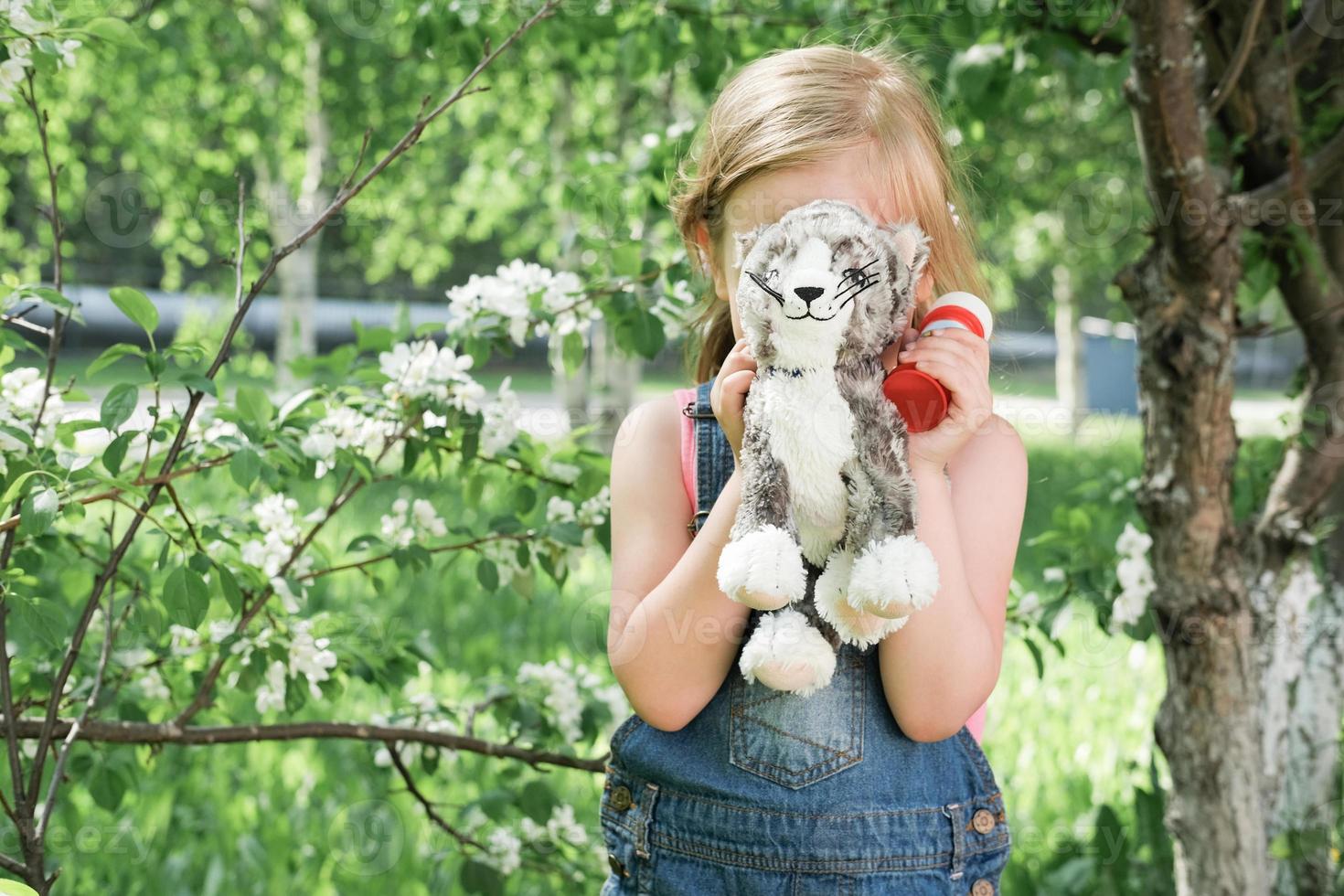 cute little girl hiding behind toy cat. blonde girl hides her face photo
